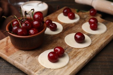 Photo of Process of making dumplings (varenyky) with cherries. Raw dough and ingredients on wooden table, closeup