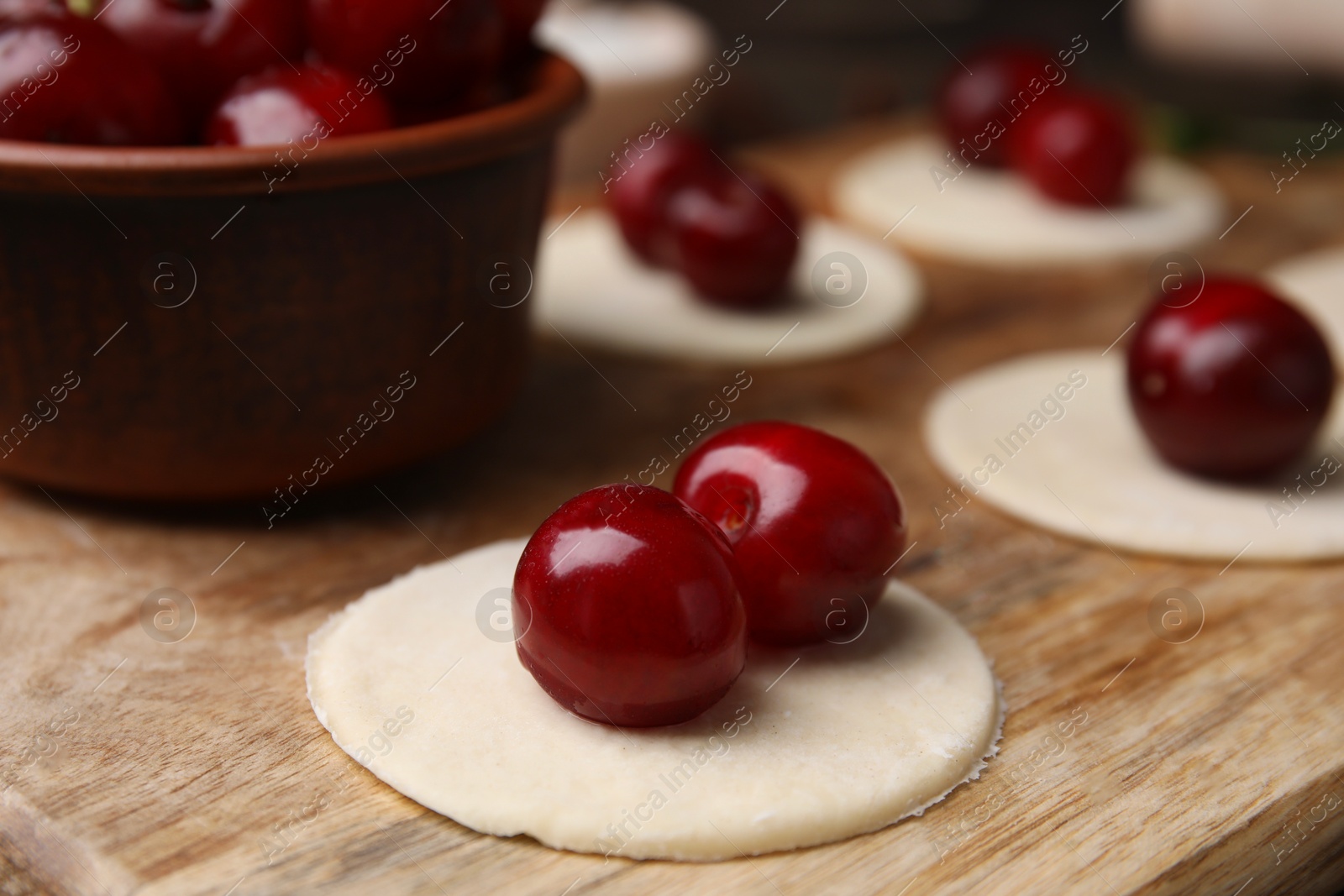 Photo of Process of making dumplings (varenyky) with cherries. Raw dough and ingredients on wooden table, closeup