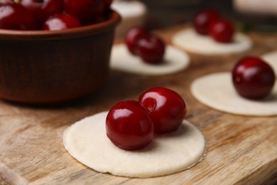 Photo of Process of making dumplings (varenyky) with cherries. Raw dough and ingredients on wooden table, closeup