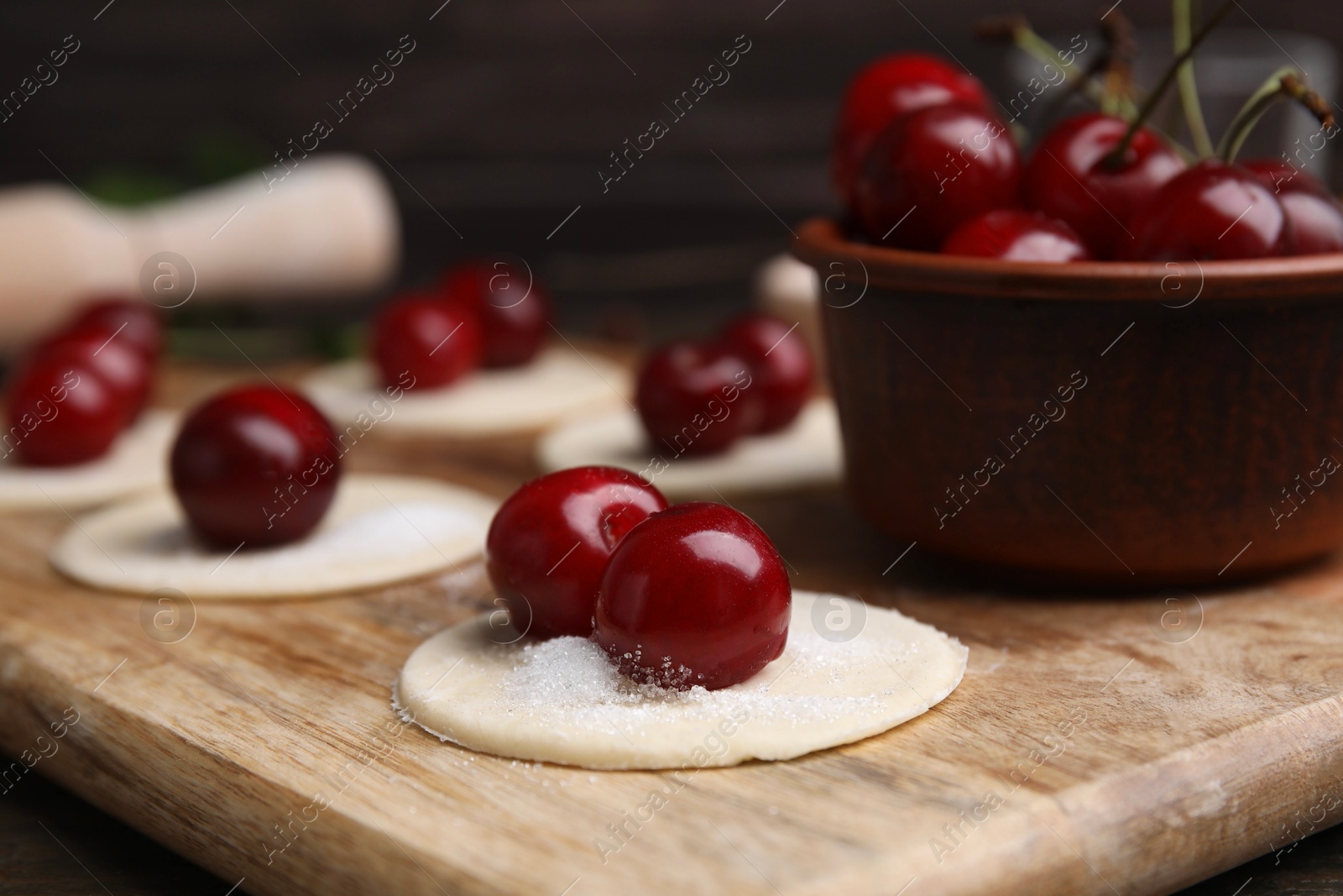 Photo of Process of making dumplings (varenyky) with cherries. Raw dough and ingredients on wooden table, closeup