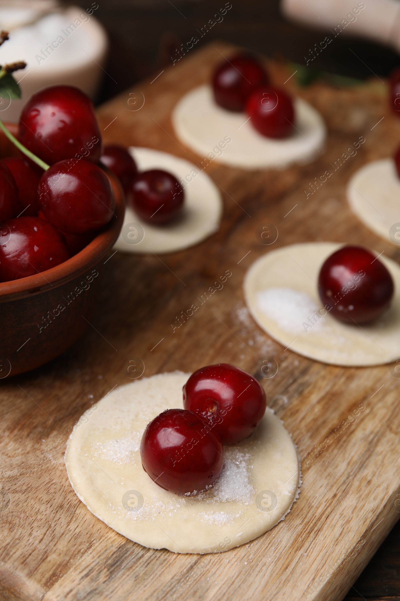 Photo of Process of making dumplings (varenyky) with cherries. Raw dough and ingredients on wooden table, closeup