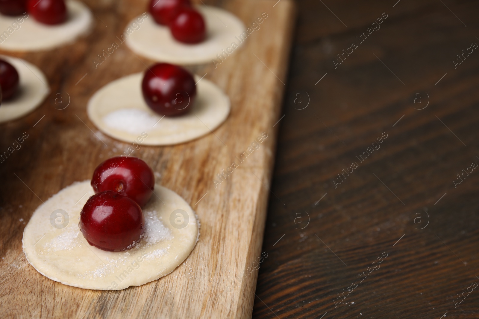 Photo of Process of making dumplings (varenyky) with cherries. Raw dough and ingredients on wooden table, closeup. Space for text