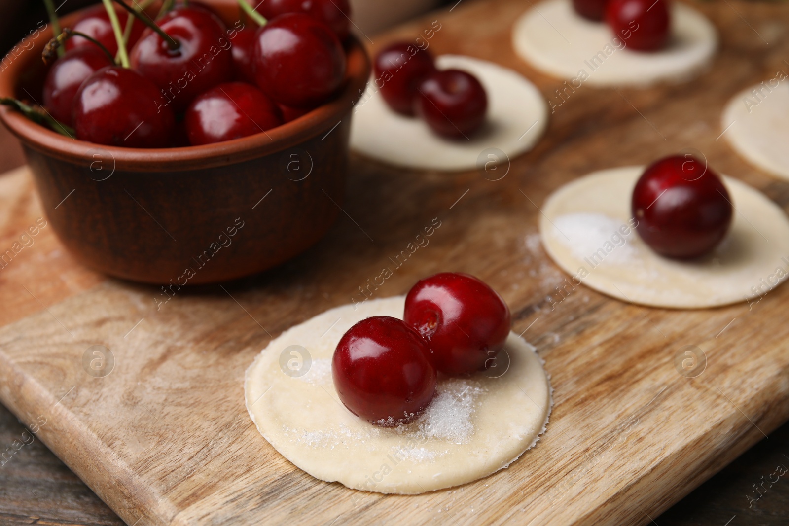 Photo of Process of making dumplings (varenyky) with cherries. Raw dough and ingredients on wooden table, closeup