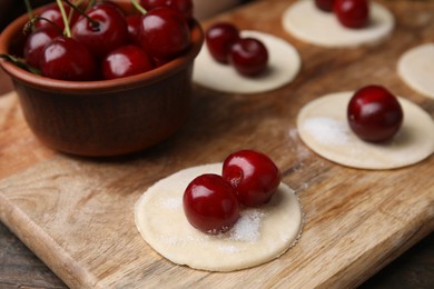 Photo of Process of making dumplings (varenyky) with cherries. Raw dough and ingredients on wooden table, closeup