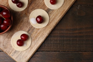 Photo of Process of making dumplings (varenyky) with cherries. Raw dough and ingredients on wooden table, top view. Space for text