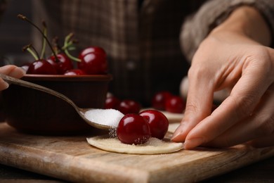 Photo of Woman making dumplings (varenyky) with cherries at wooden table, closeup
