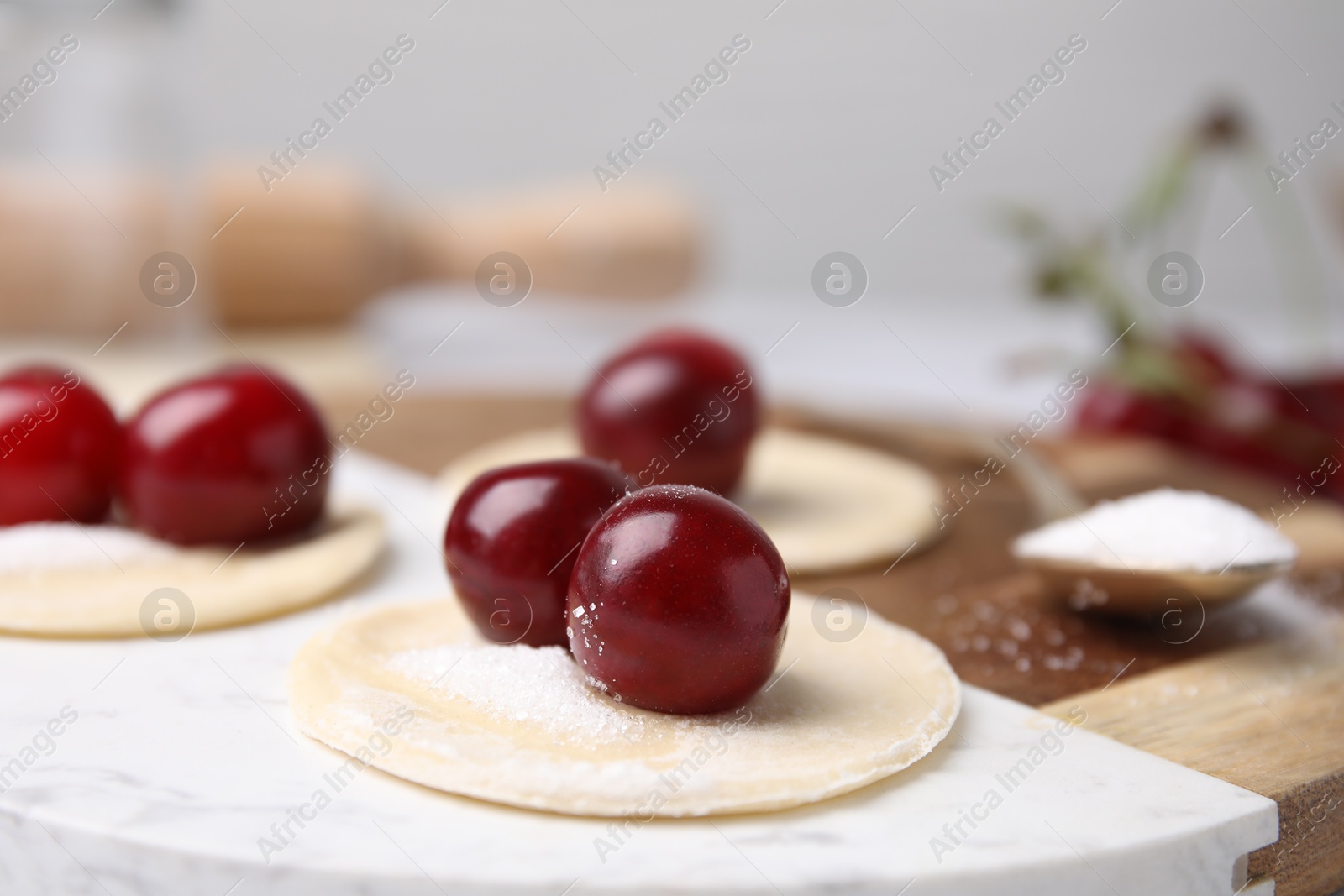 Photo of Process of making dumplings (varenyky) with cherries. Raw dough and ingredients on white table, closeup