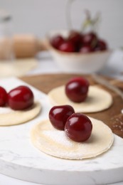 Photo of Process of making dumplings (varenyky) with cherries. Raw dough and ingredients on white table, closeup