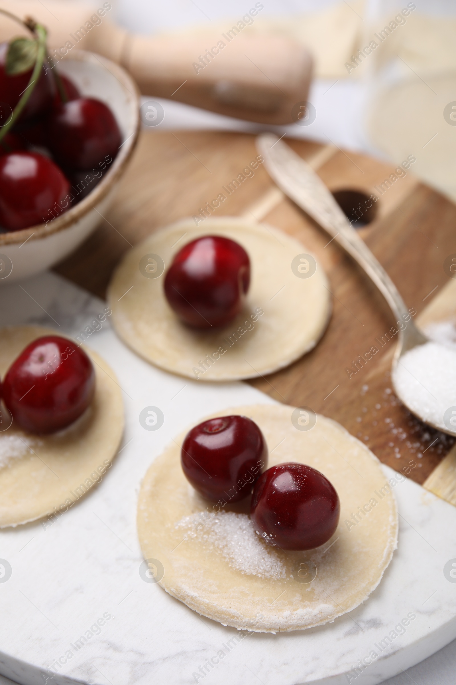 Photo of Process of making dumplings (varenyky) with cherries. Raw dough and ingredients on white tiled table, closeup