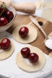 Photo of Process of making dumplings (varenyky) with cherries. Raw dough and ingredients on white tiled table, closeup