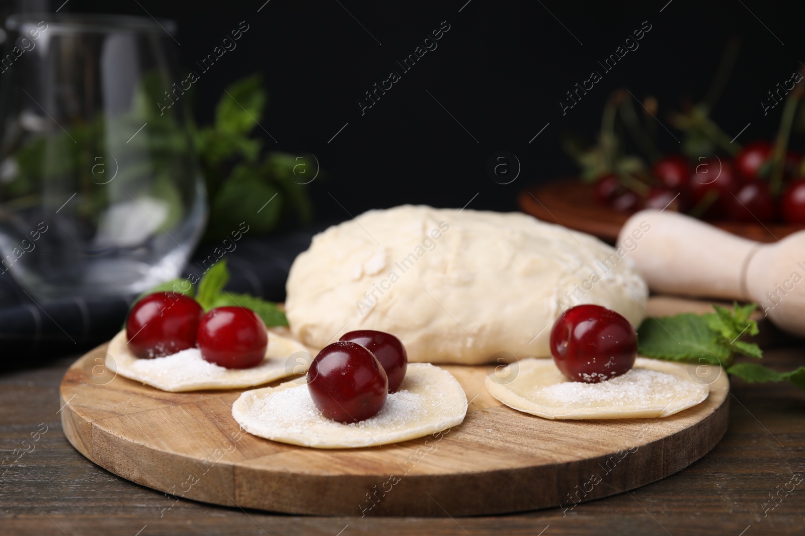 Photo of Process of making dumplings (varenyky) with cherries. Raw dough and ingredients on wooden table