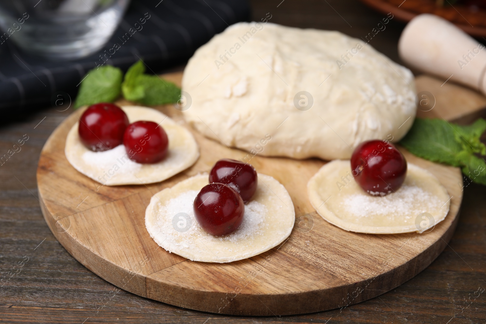 Photo of Process of making dumplings (varenyky) with cherries. Raw dough and ingredients on wooden table, closeup