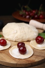 Process of making dumplings (varenyky) with cherries. Raw dough and ingredients on wooden table, closeup