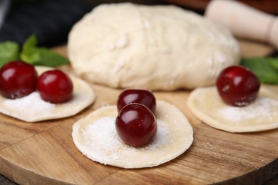 Photo of Process of making dumplings (varenyky) with cherries. Raw dough and ingredients on wooden table, closeup