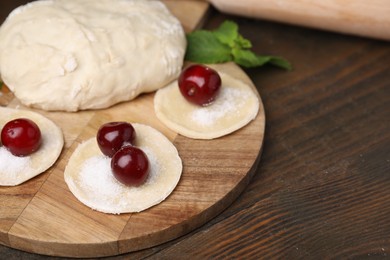 Photo of Process of making dumplings (varenyky) with cherries. Raw dough and ingredients on wooden table, closeup