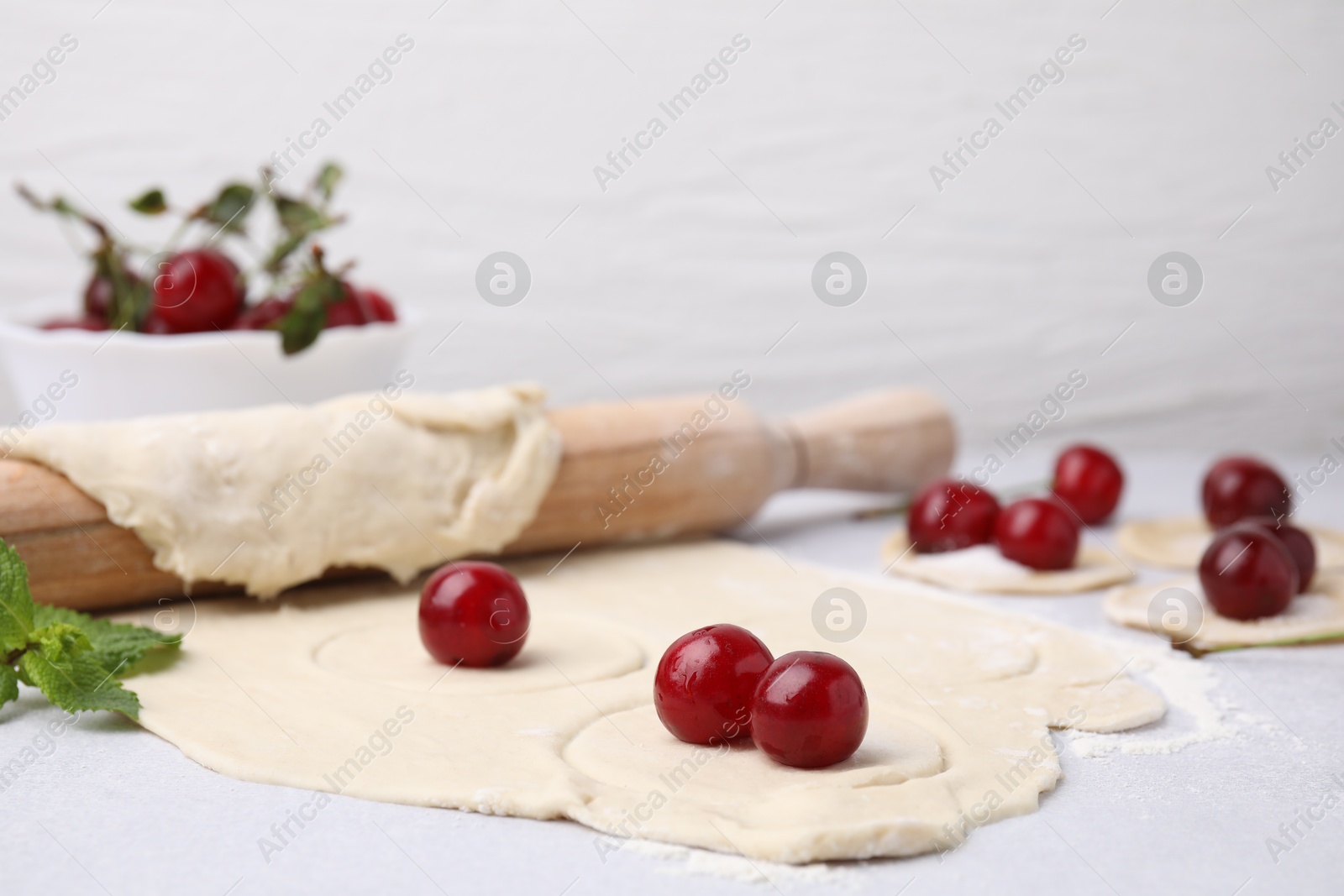 Photo of Process of making dumplings (varenyky) with cherries. Raw dough and ingredients on light table