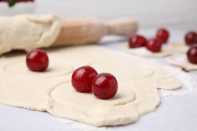 Photo of Process of making dumplings (varenyky) with cherries. Raw dough and ingredients on light table, closeup