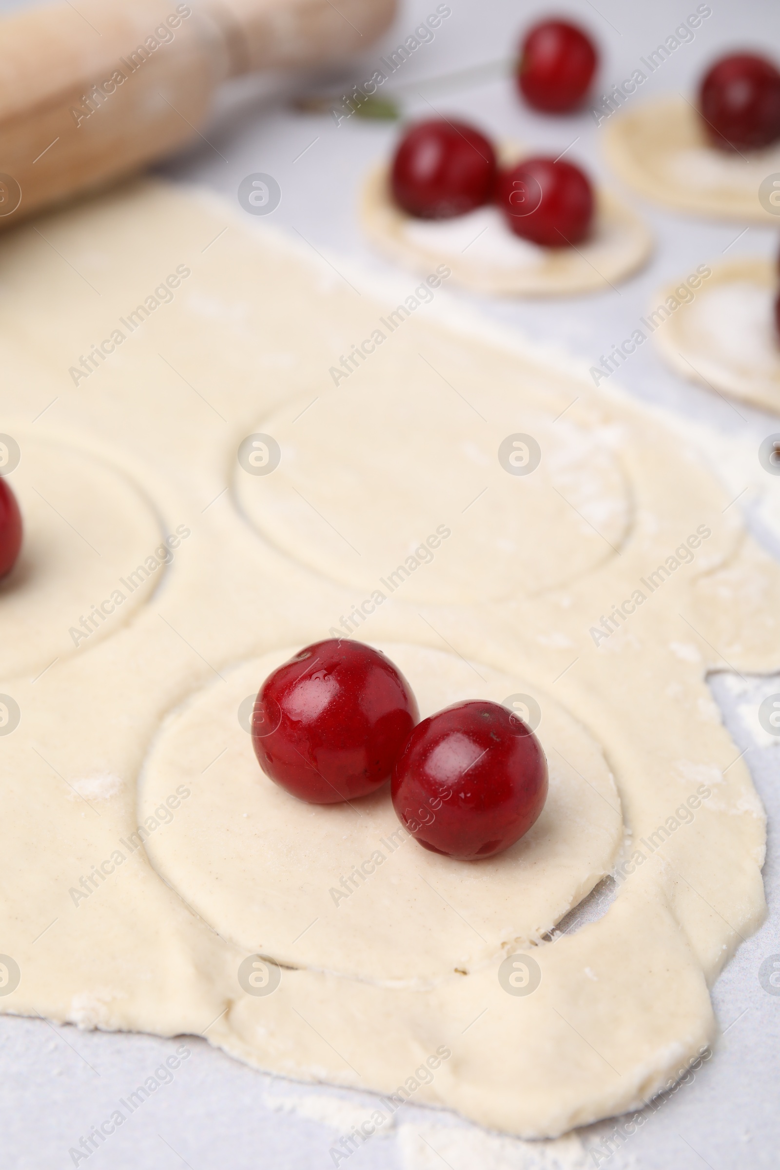 Photo of Process of making dumplings (varenyky) with cherries. Raw dough and ingredients on light table, closeup