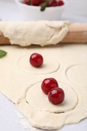 Photo of Process of making dumplings (varenyky) with cherries. Raw dough and ingredients on light table, closeup