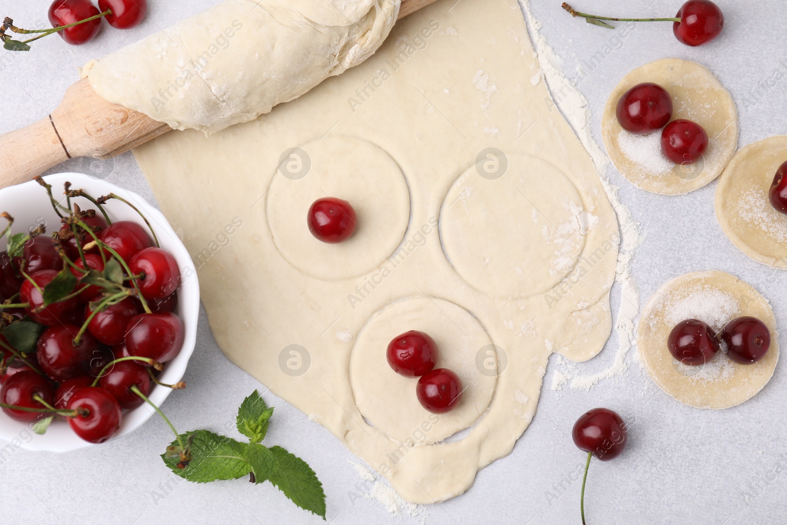 Photo of Process of making dumplings (varenyky) with cherries. Raw dough and ingredients on light table, flat lay