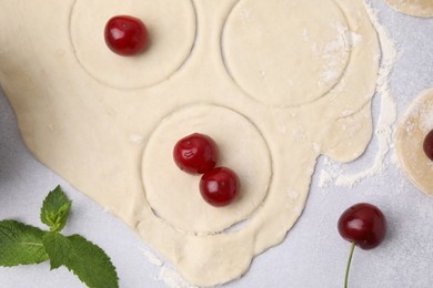 Process of making dumplings (varenyky) with cherries. Raw dough and ingredients on light table, flat lay