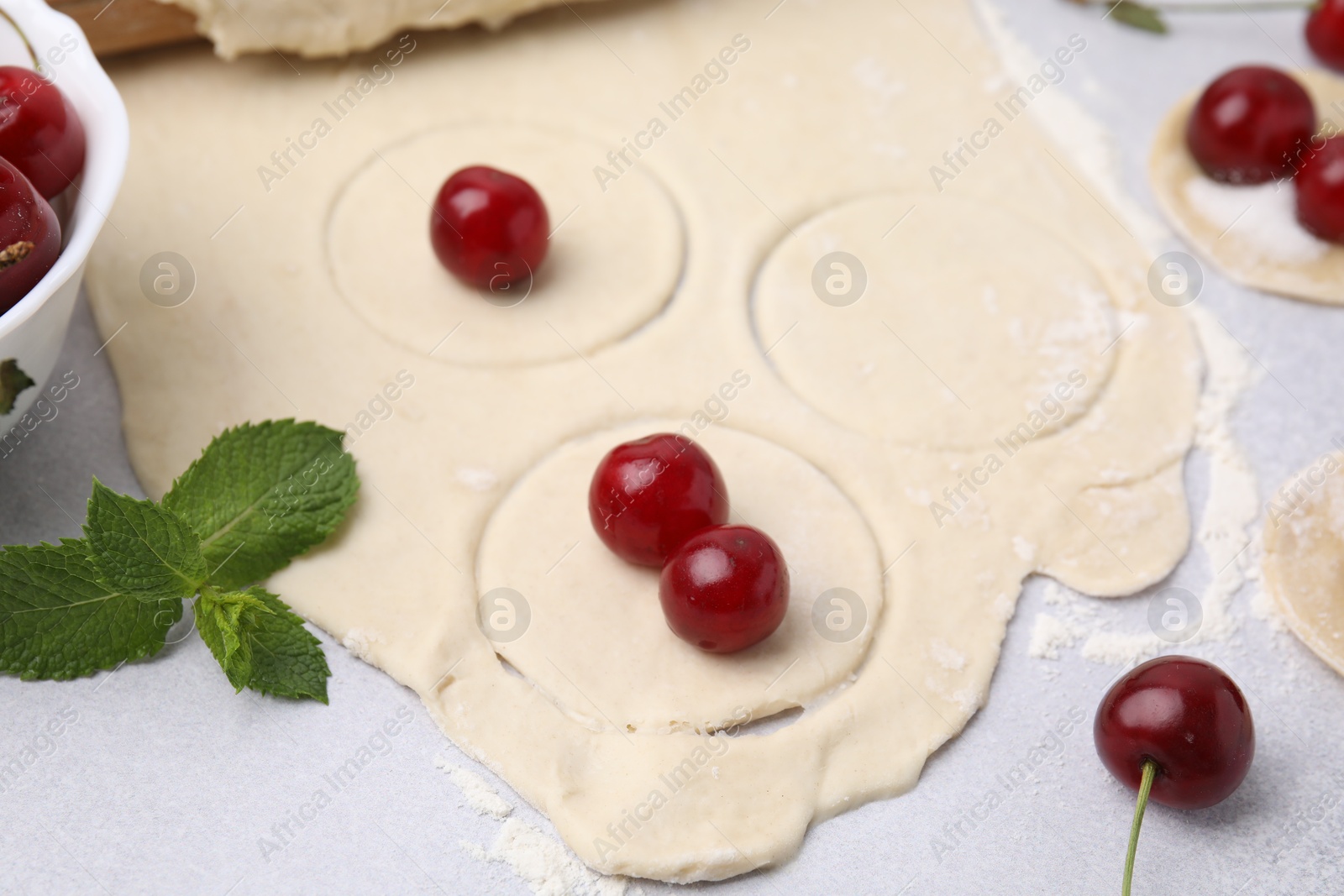 Photo of Process of making dumplings (varenyky) with cherries. Raw dough and ingredients on light table, closeup