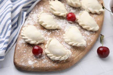 Photo of Raw dumplings (varenyky) and fresh cherries on white tiled table, closeup