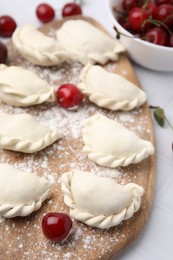 Photo of Raw dumplings (varenyky) and fresh cherries on white tiled table, closeup