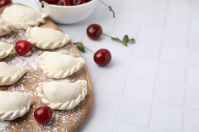 Photo of Raw dumplings (varenyky) and fresh cherries on white tiled table, closeup. Space for text