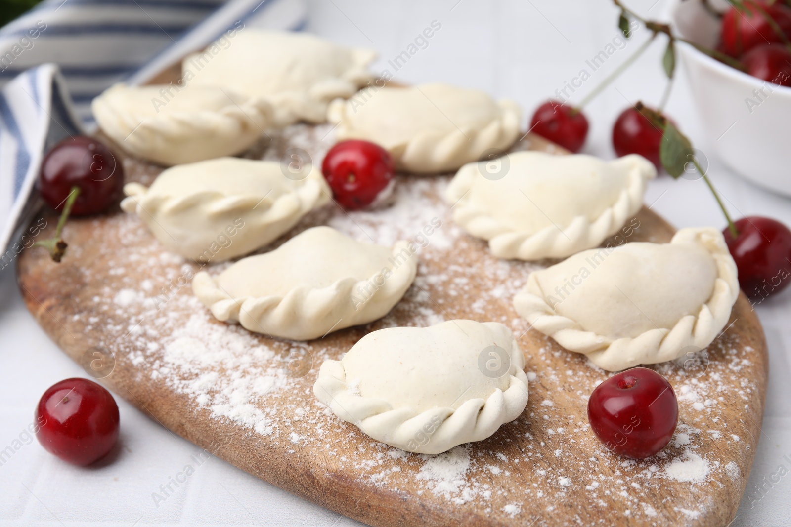 Photo of Raw dumplings (varenyky) and fresh cherries on white tiled table, closeup