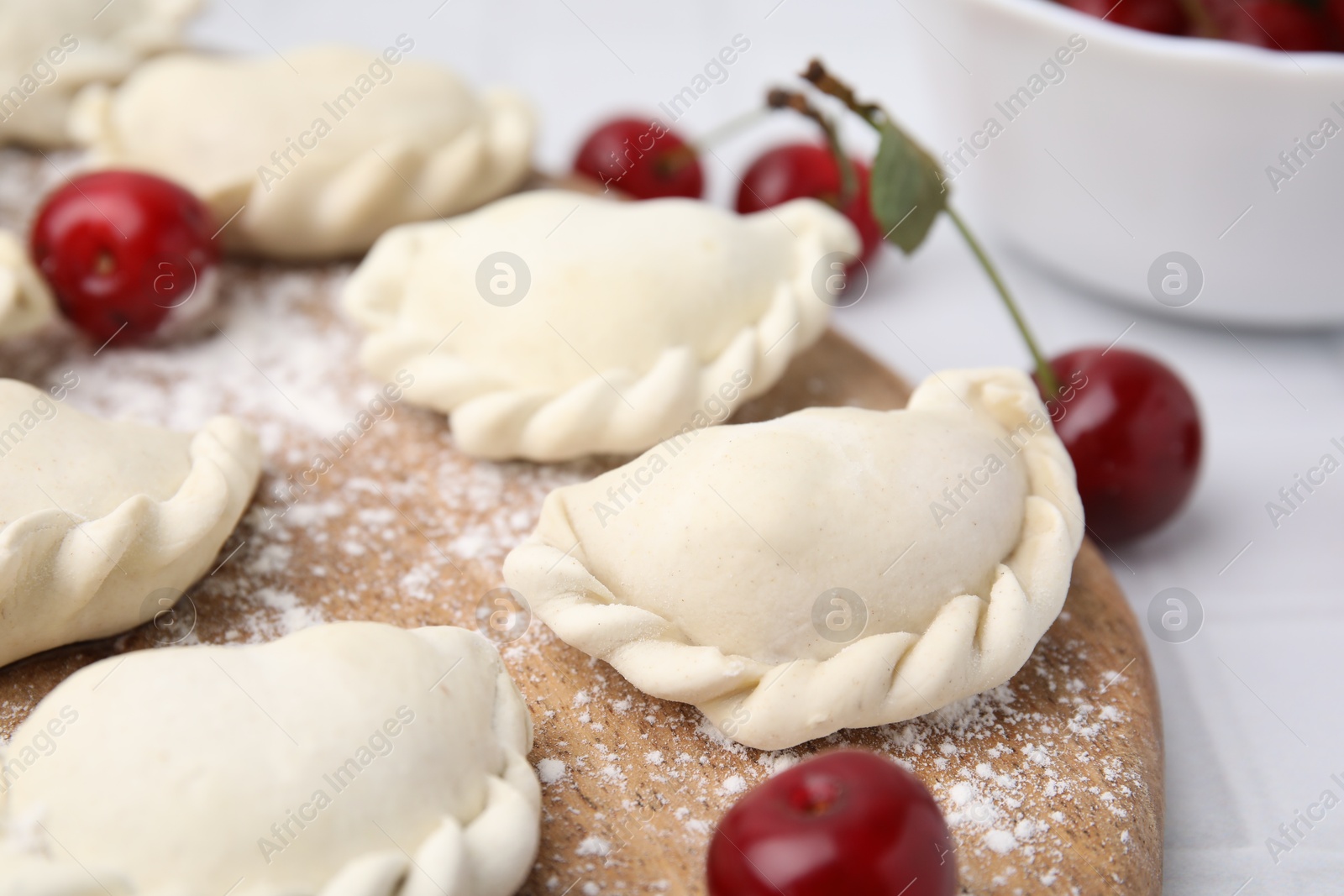 Photo of Raw dumplings (varenyky) and fresh cherries on white tiled table, closeup