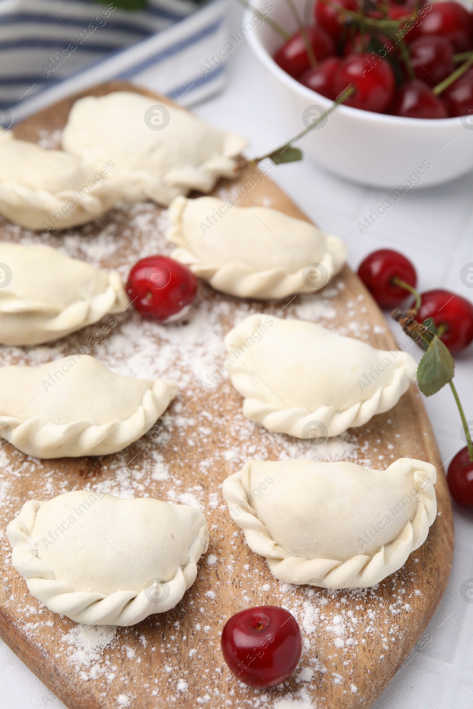 Photo of Raw dumplings (varenyky) and fresh cherries on white tiled table, closeup