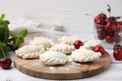 Raw dumplings (varenyky) and fresh cherries on white wooden table