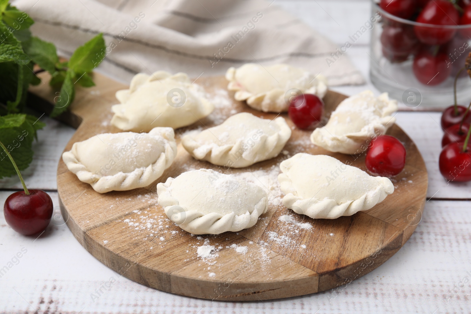 Photo of Raw dumplings (varenyky) and fresh cherries on white wooden table