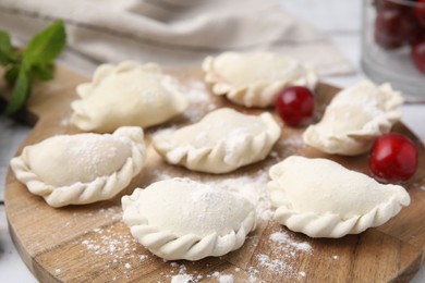 Photo of Raw dumplings (varenyky) and fresh cherries on table, closeup