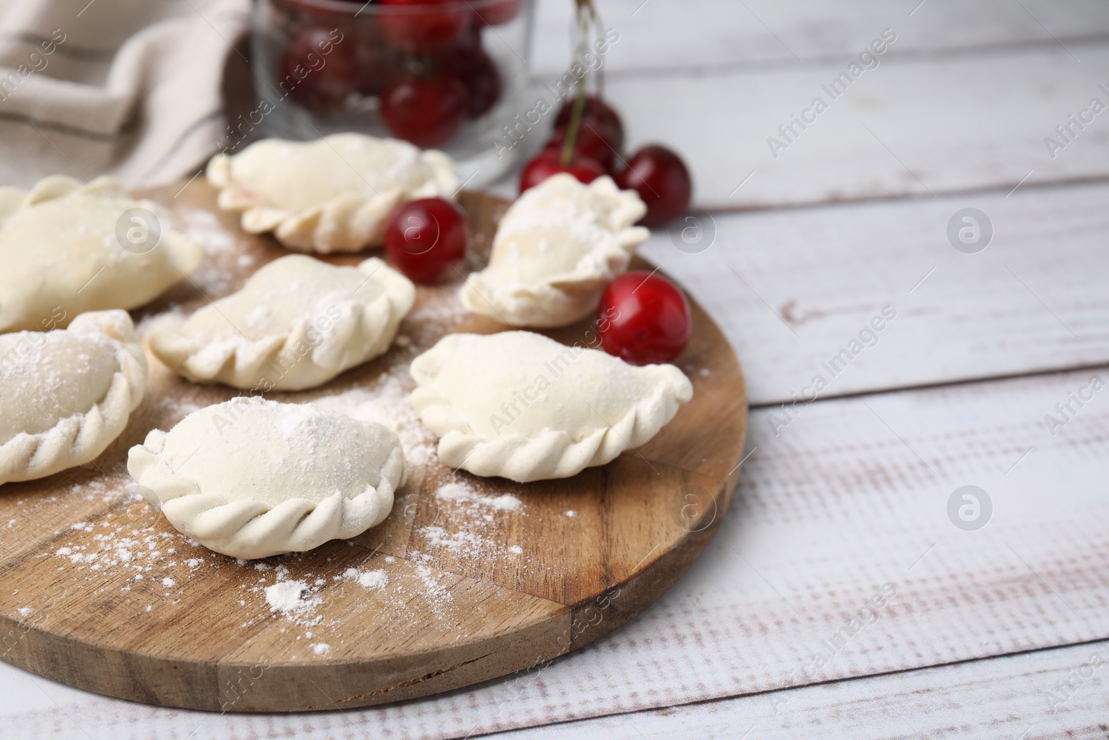 Photo of Raw dumplings (varenyky) and fresh cherries on white wooden table. Space for text