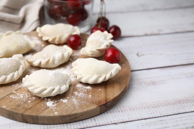 Photo of Raw dumplings (varenyky) and fresh cherries on white wooden table. Space for text