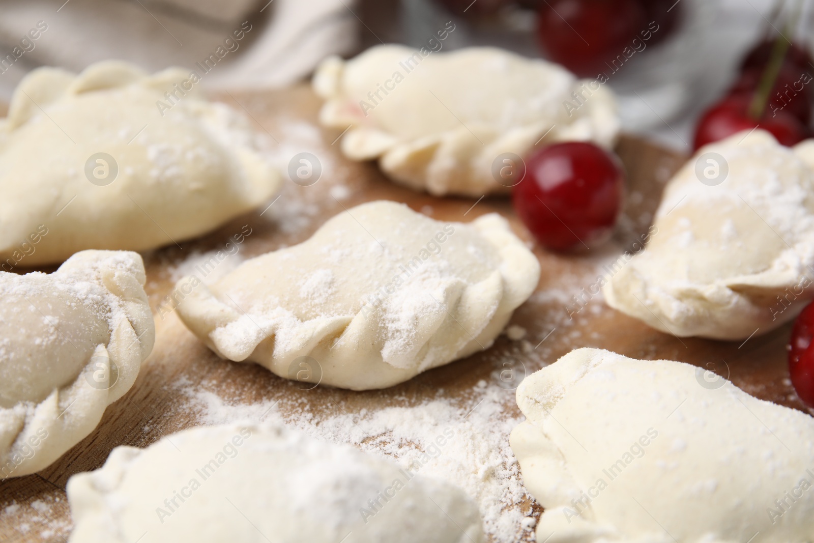 Photo of Raw dumplings (varenyky) and fresh cherries on table, closeup