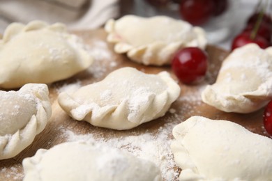 Photo of Raw dumplings (varenyky) and fresh cherries on table, closeup