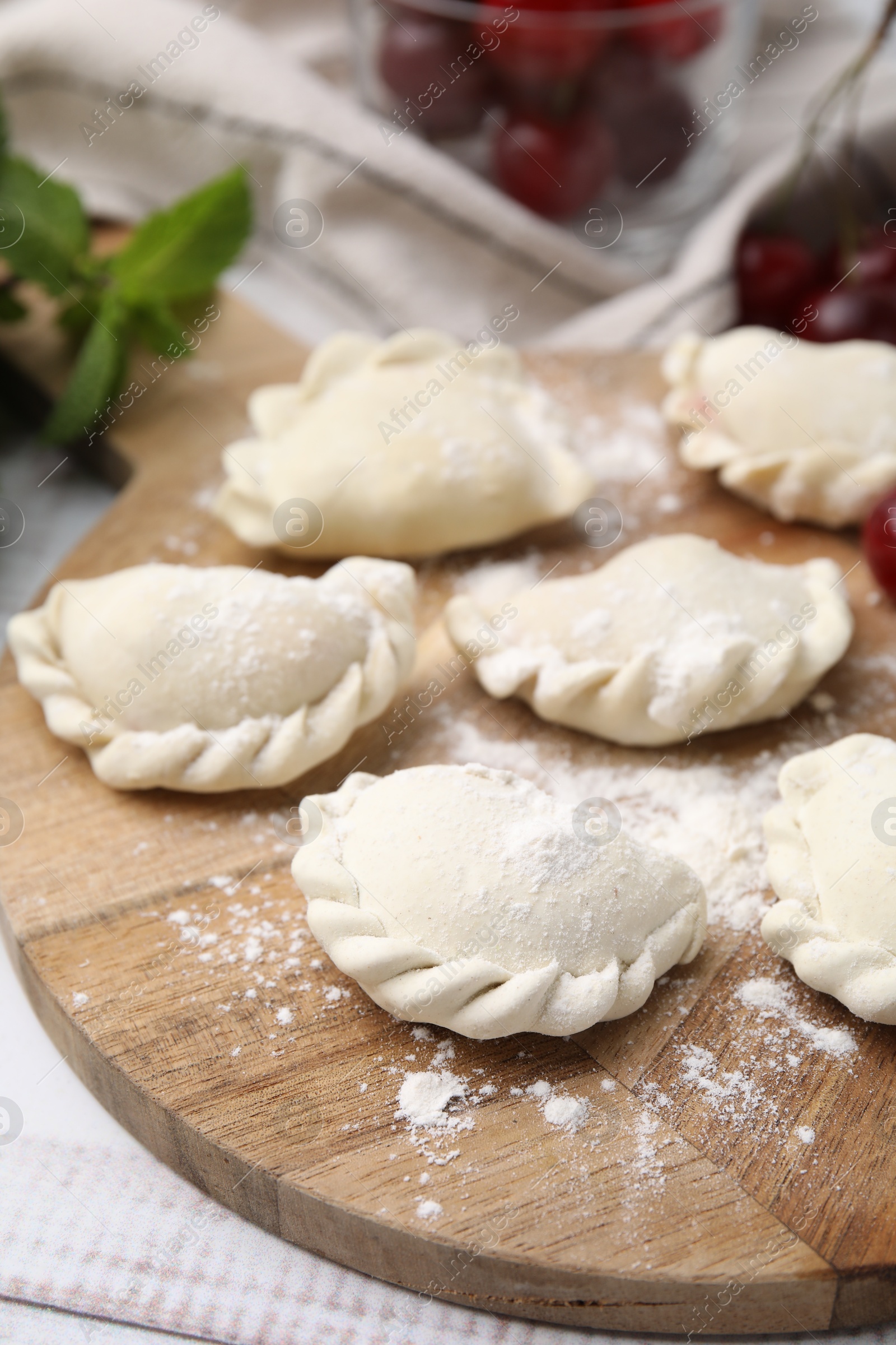 Photo of Raw dumplings (varenyky) and fresh cherries on white wooden table, closeup