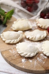 Raw dumplings (varenyky) and fresh cherries on white wooden table, closeup