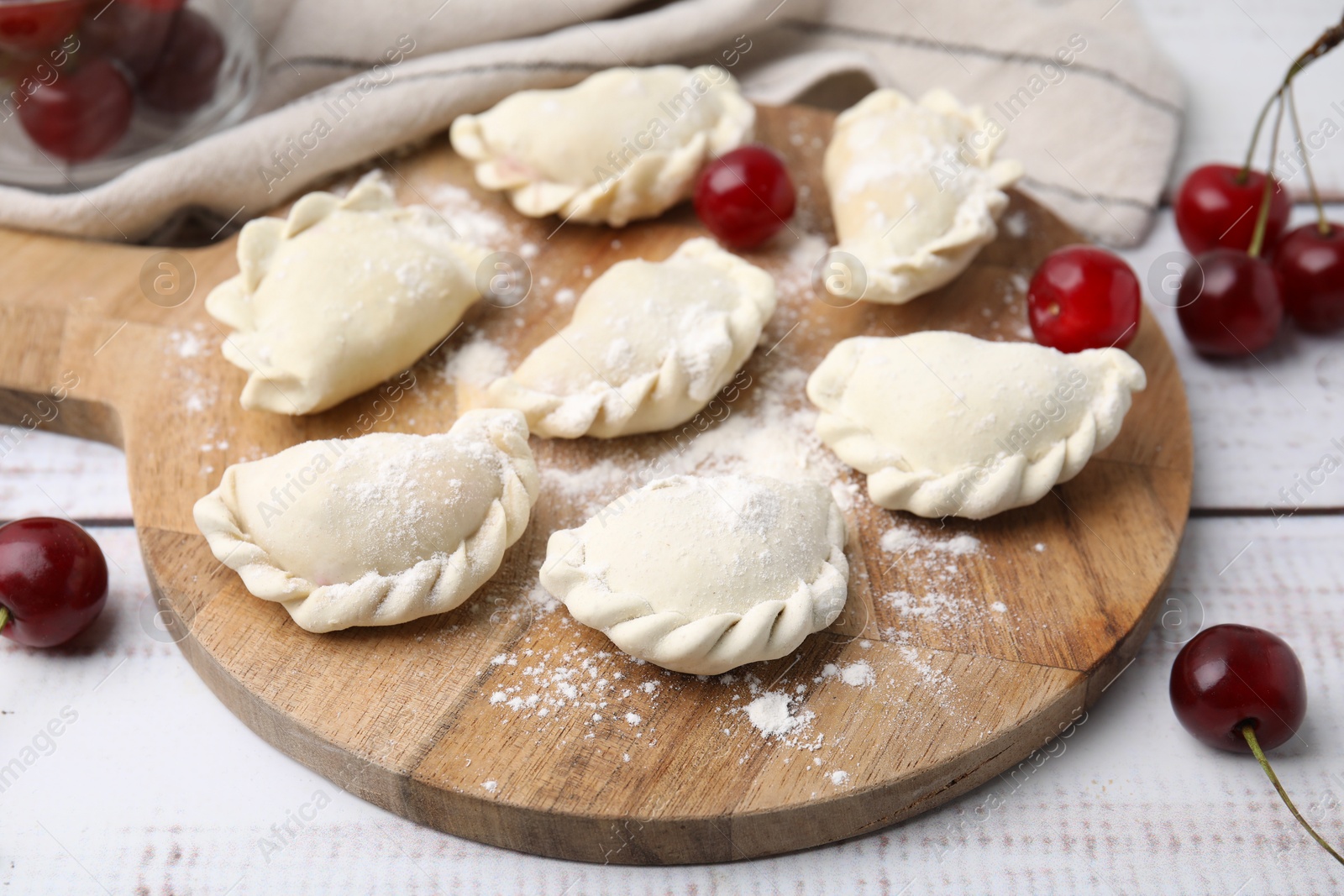 Photo of Raw dumplings (varenyky) and fresh cherries on white wooden table