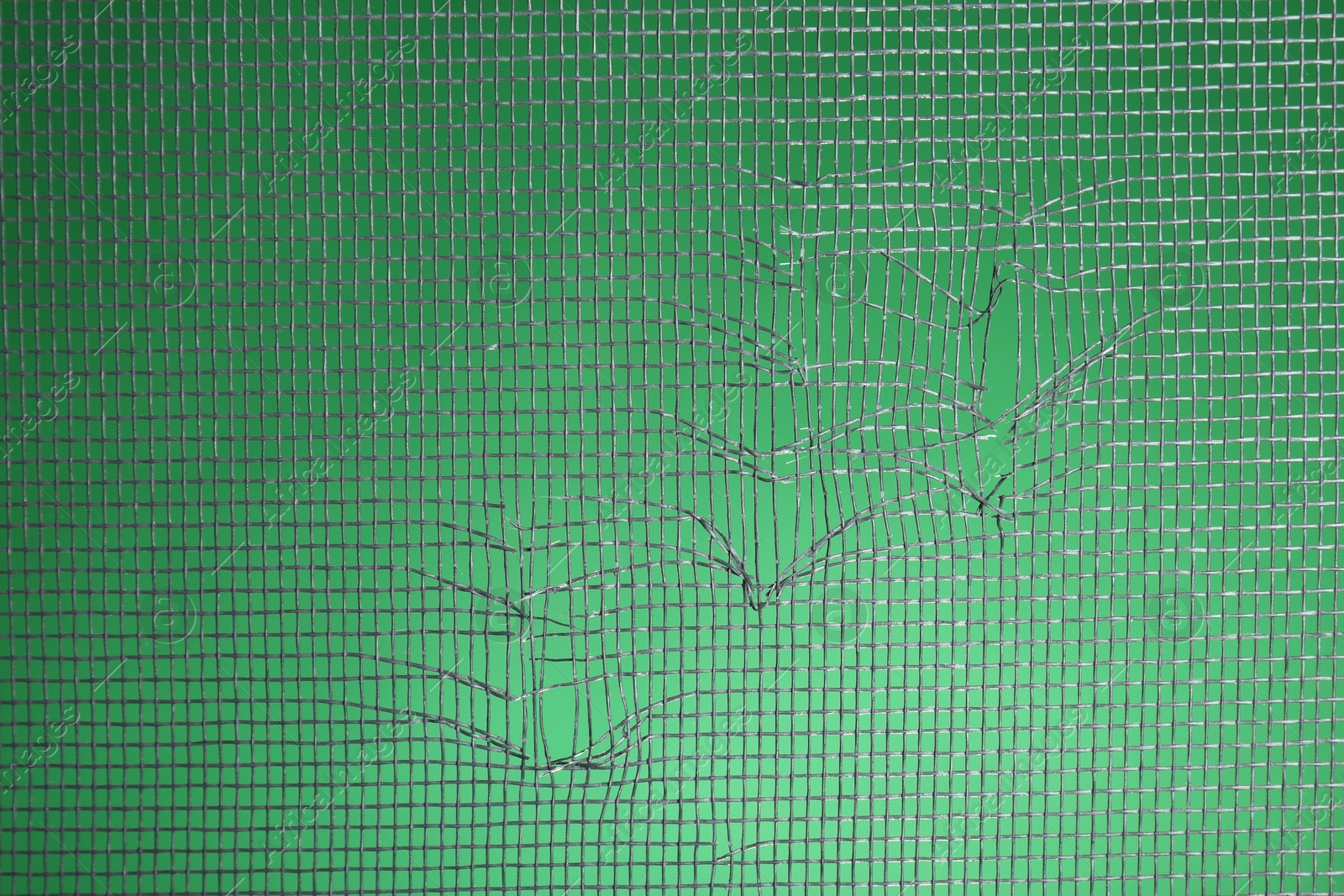 Photo of Torn window screen against green background, closeup