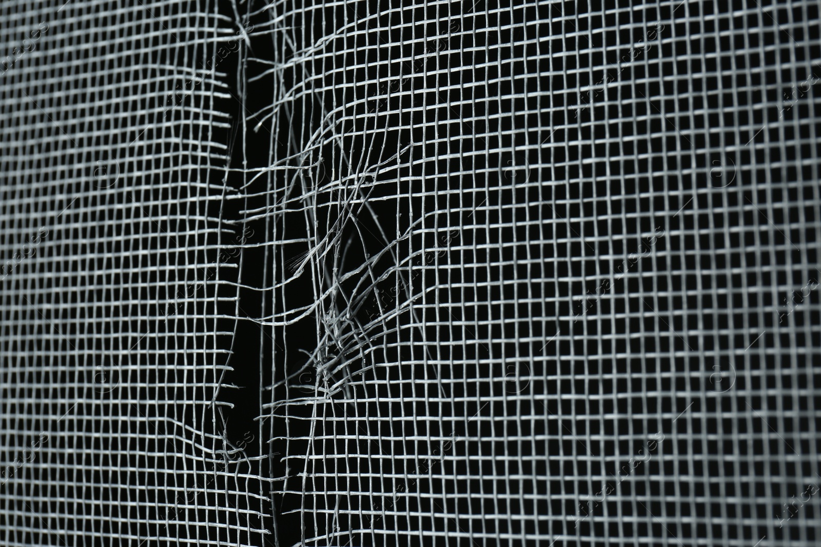 Photo of Torn window screen against black background, closeup