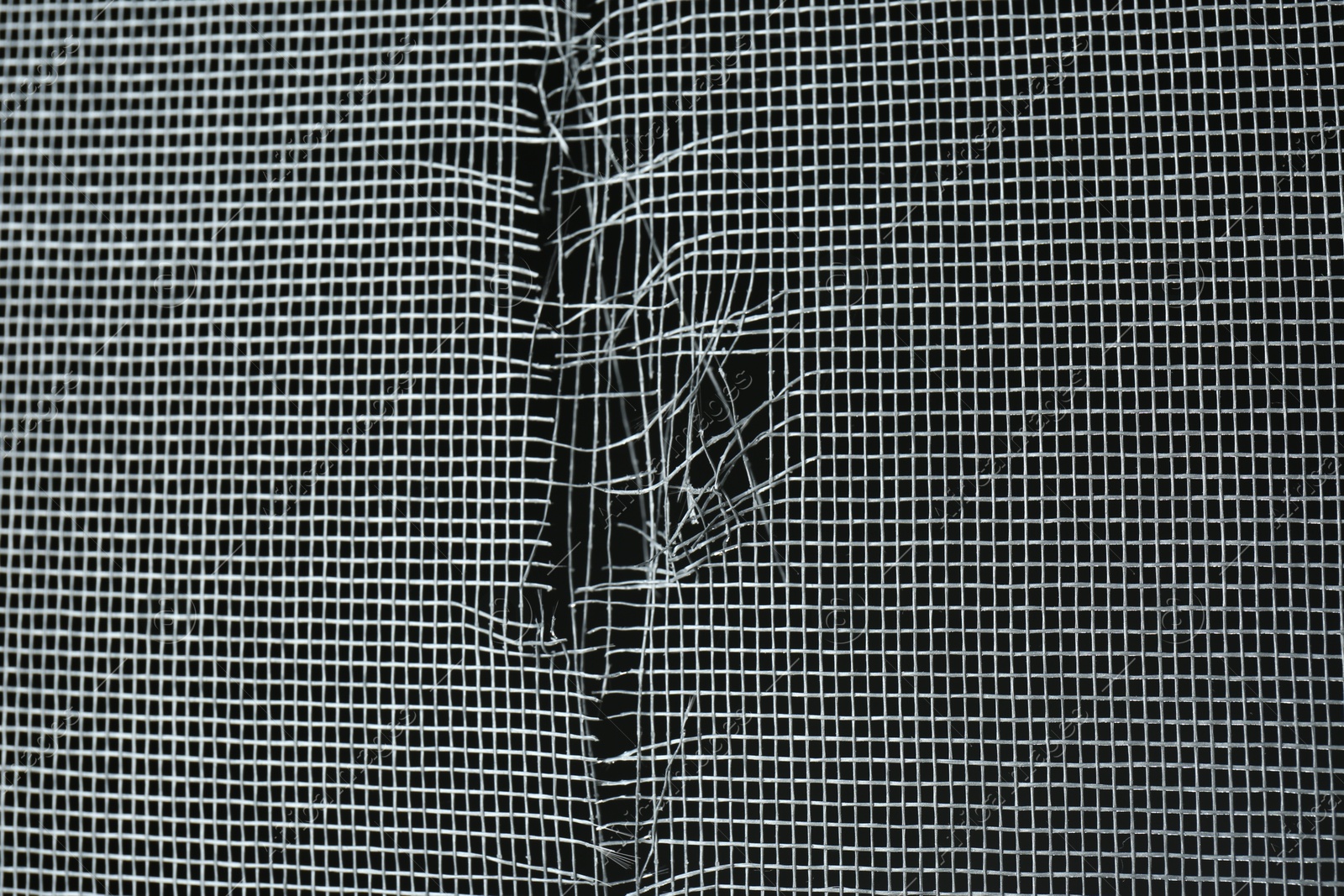 Photo of Torn window screen against black background, closeup