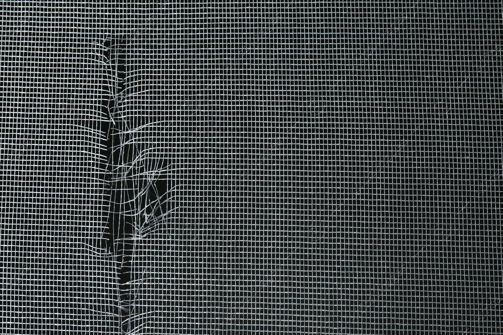 Photo of Torn window screen against black background, closeup