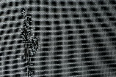 Photo of Torn window screen against black background, closeup