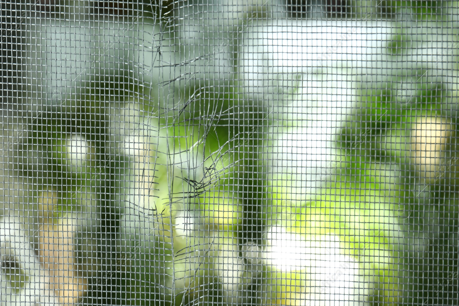 Photo of Torn window screen against blurred background, closeup