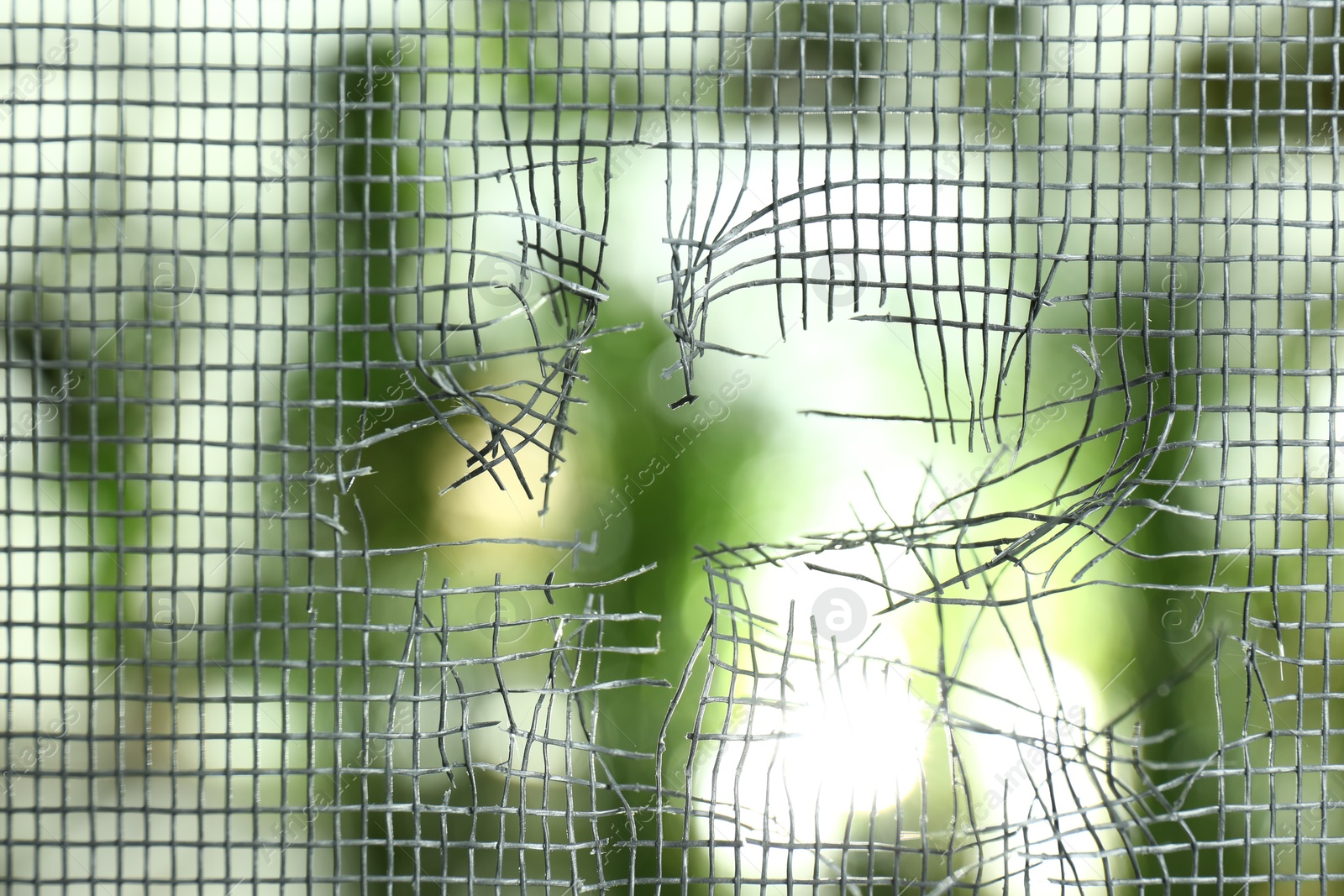 Photo of Torn window screen against blurred background, closeup