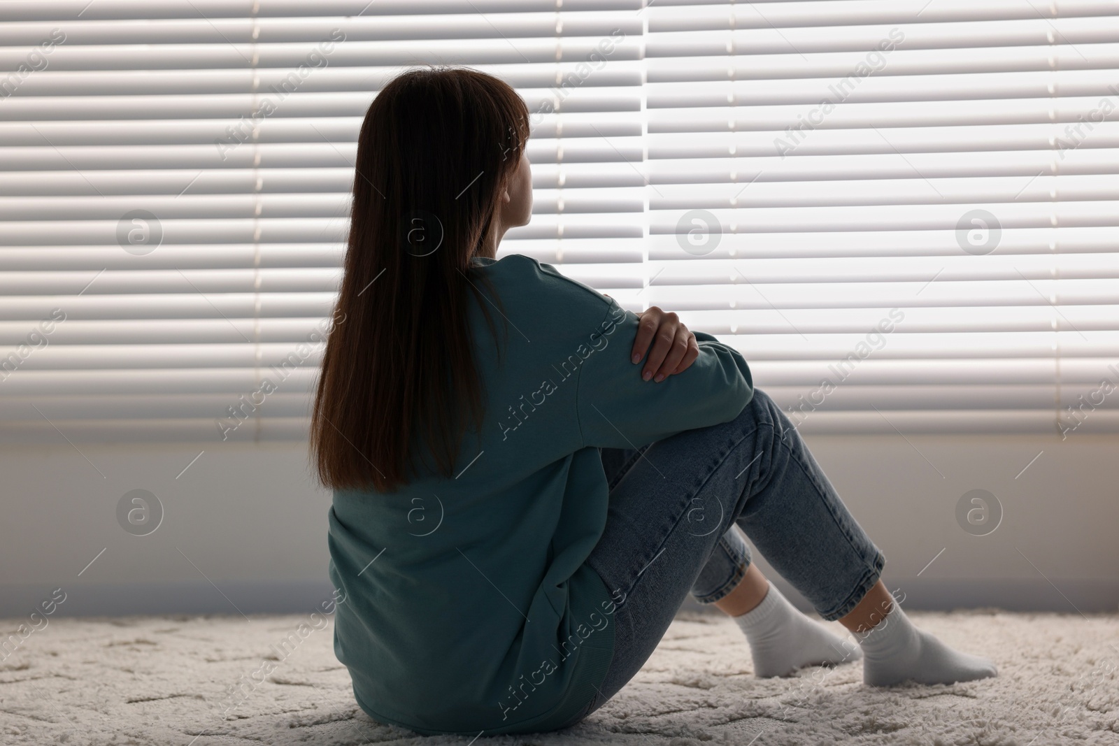 Photo of Loneliness concept. Sad woman sitting on floor at home, back view